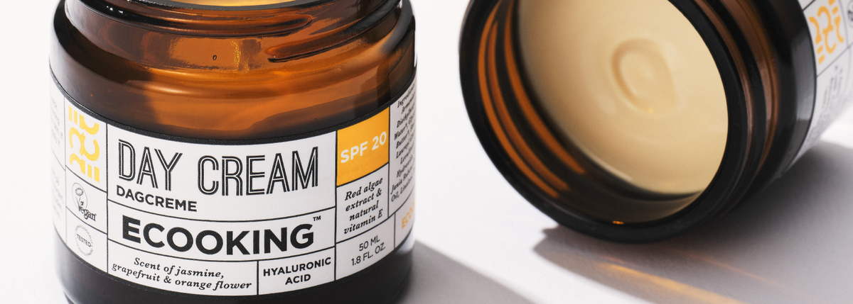 Nærbillede af en krukke ECOOKING Dagcreme SPF 20 med duft af jasmin, grapefrugt og appelsinblomst, ved siden af en åben krukke, hvor cremen er synlig.