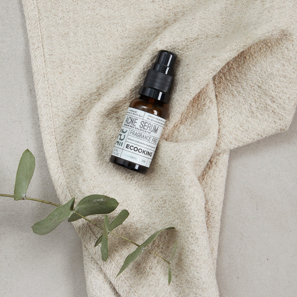 Acne Serum på et lyst håndklæde med eukalyptusgren – acne serum med salicylsyre mod bumser, uren hud og store porer