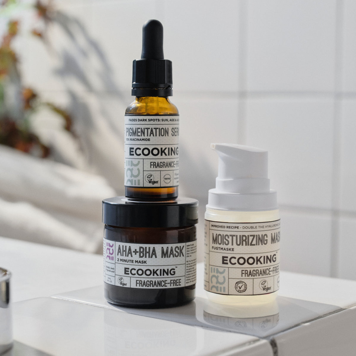 ECOOKING AHA+BHA Maske med Pigment Serum ovenpå og Fugtmaske ved siden af på en badeværelseshylde – kemisk peeling maske med AHA og BHA mod pigmentpletter
