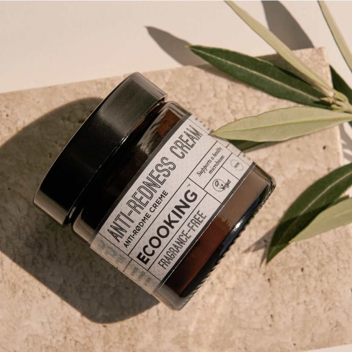 Krukke med Anti-rødme Creme på en sandstensplade med olivengrene – creme mod rødme og pleje til sensitiv hud med rosacea