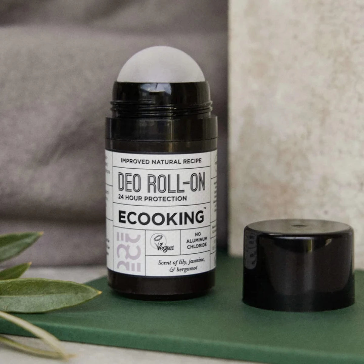 ECOOKING Deo Roll-on i sort beholder med låget af på en grøn bog ved siden af olivengrene – naturlig deodorant uden aluminium til kvinder