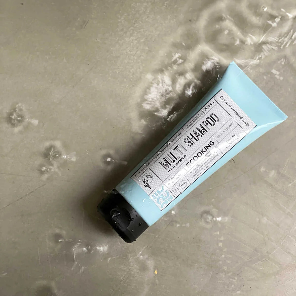 ECOOKING Multi Shampoo i lyseblå tube på et vådt gulv med vandsprøjt – shampoo til tør og kløende hovedbund, der køler og beroliger