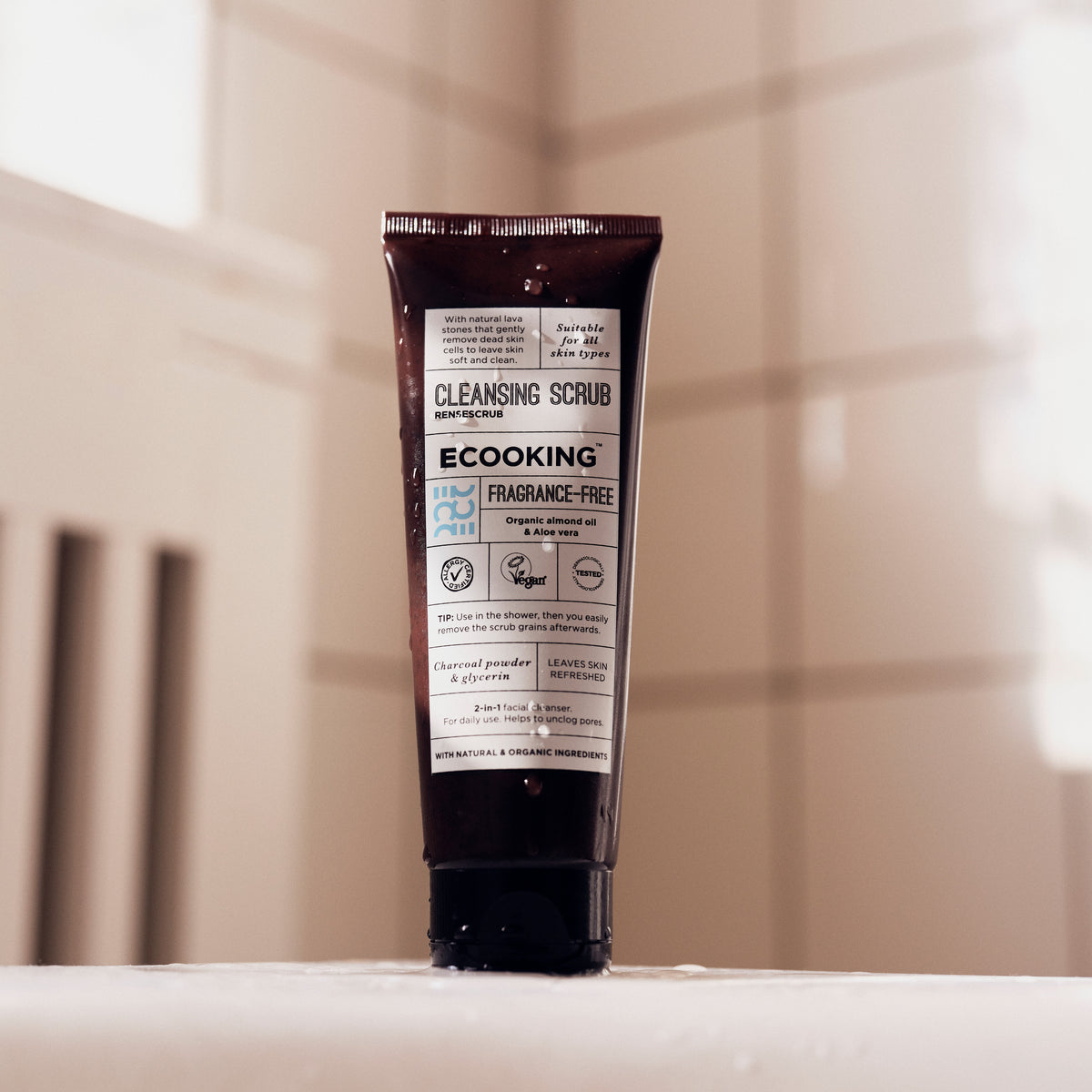 ECOOKING Rensescrub i brun tube stående på en hvid kant i et lyst badeværelse – face scrub til glat hud med frisk glød